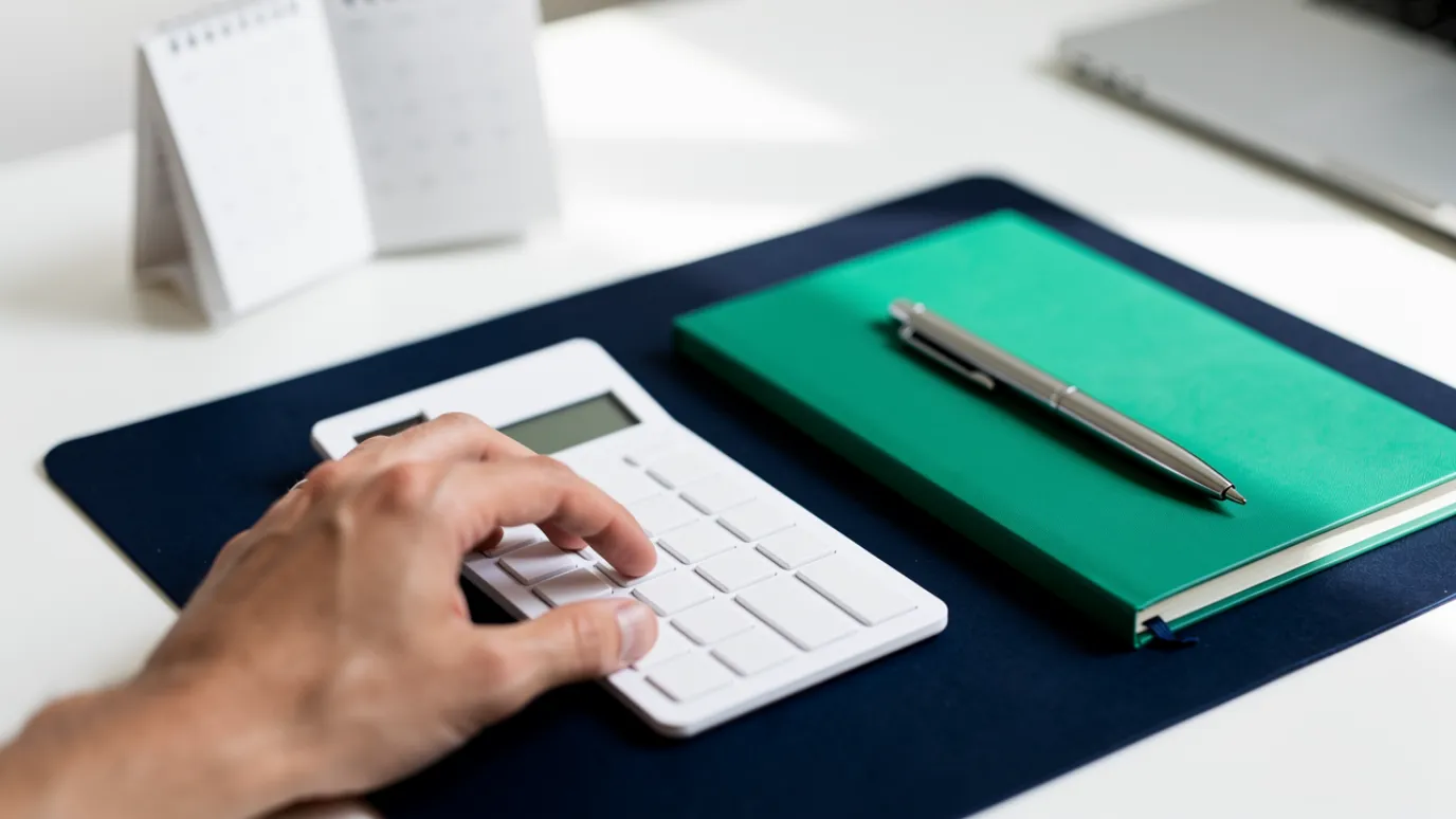 Working out on a calculator whether Coursera Plus is worth it, with a calendar and notebook on the desk